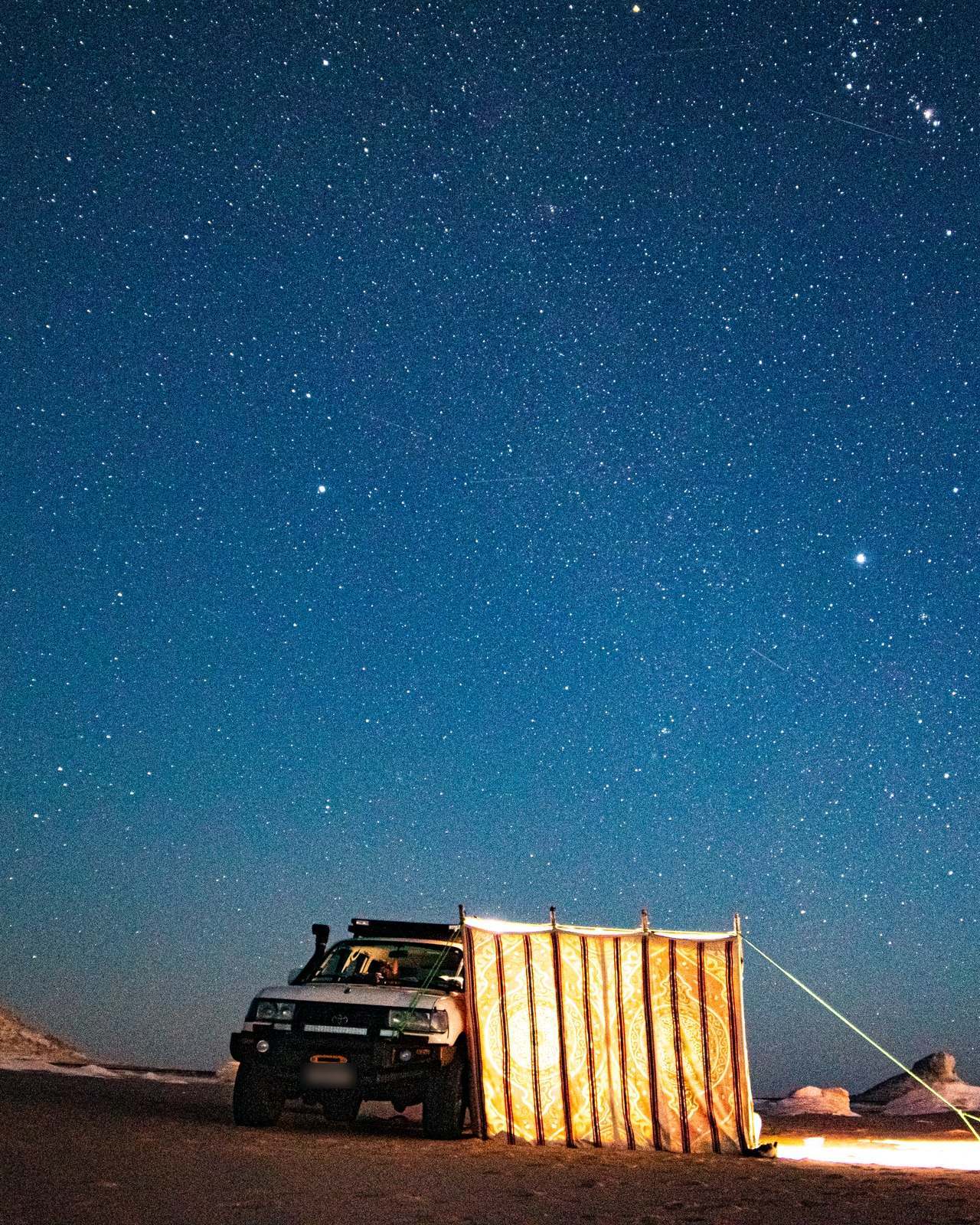 Stars over a desert camp with an off-road vehicle and a glowing tent