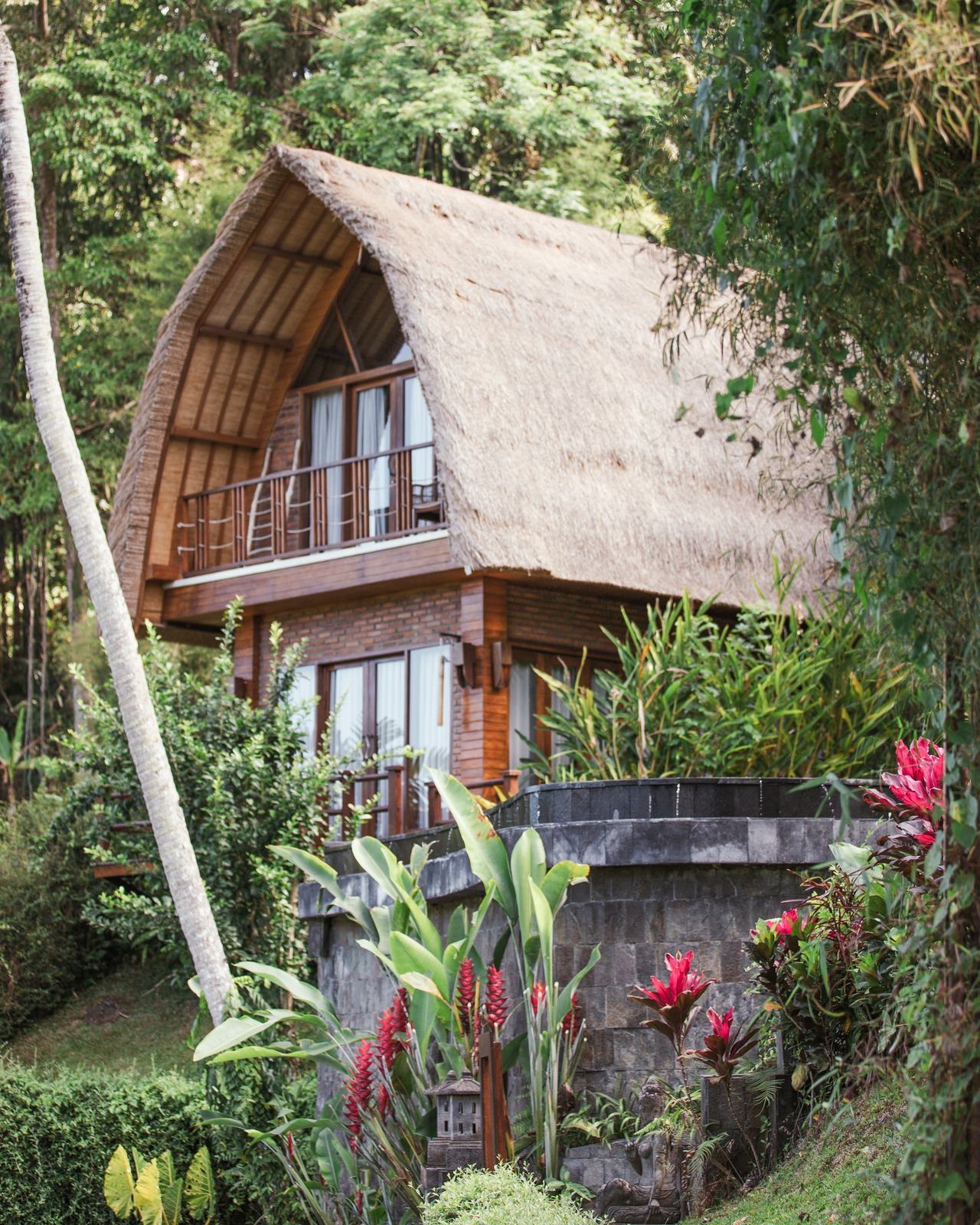 A thatched-roof villa among jungle greenery and red tropical flowers