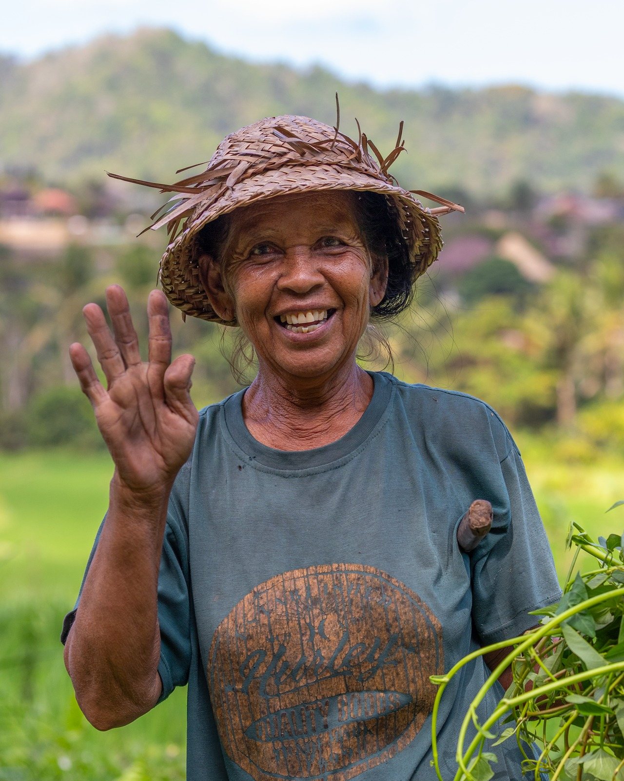 Portrait of a smiling woman in a woven hat raising her hand in greeting